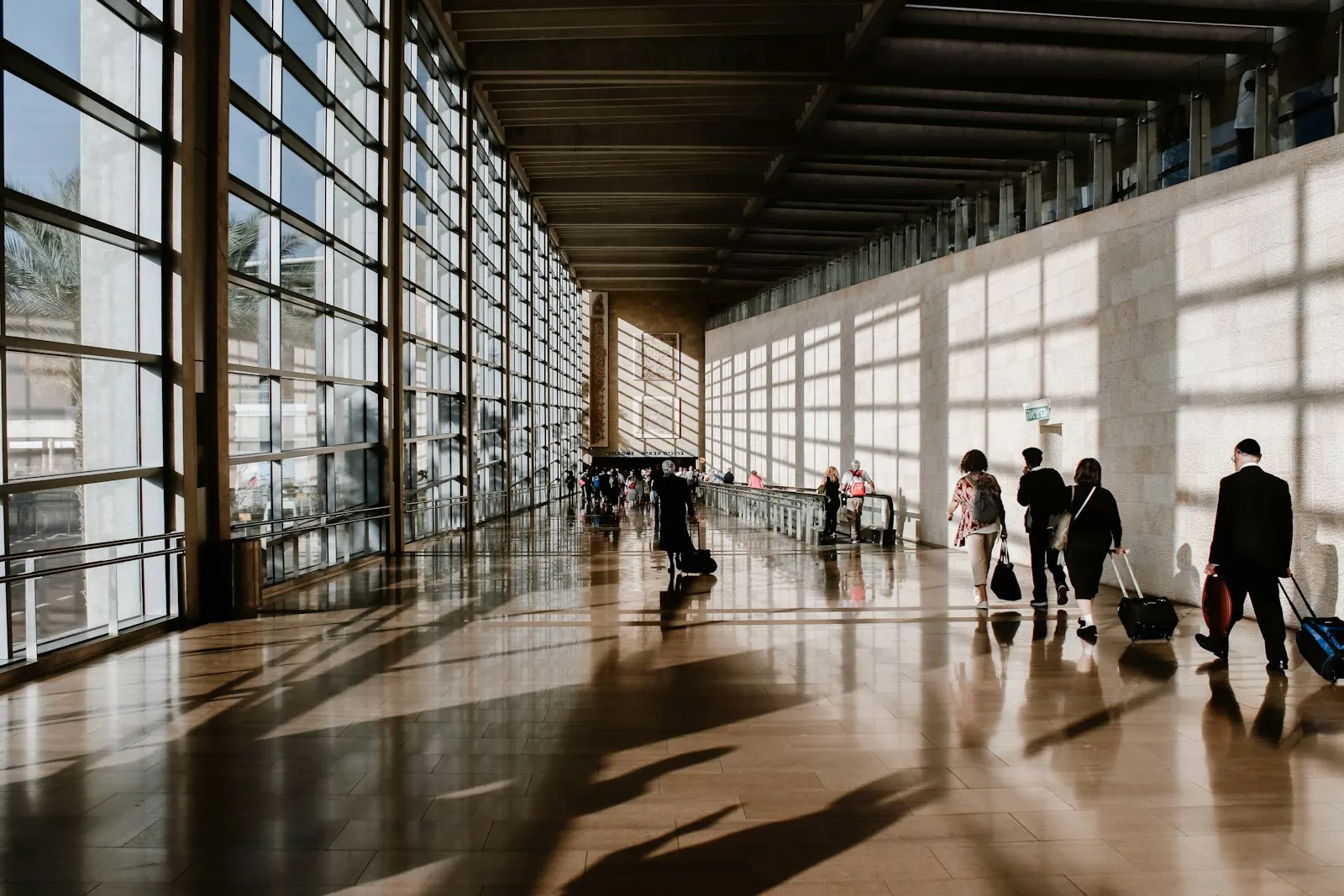 Gün ışığı alan havalimanı terminal koridorunda bavullarıyla yürüyen yolcular